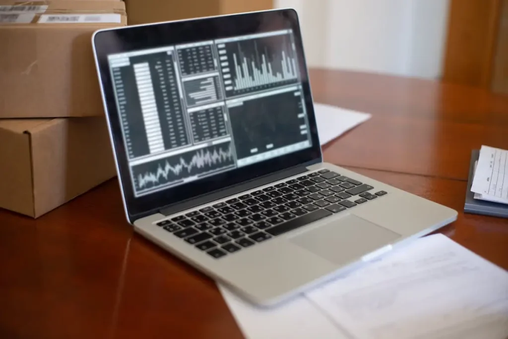 Laptop menampilkan grafik data bisnis di meja kerja dengan kotak paket, menggambarkan digitalisasi UMKM