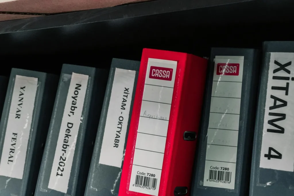 Binder berwarna-warni tertata rapi di rak penyimpanan kantor dengan label yang terorganisir